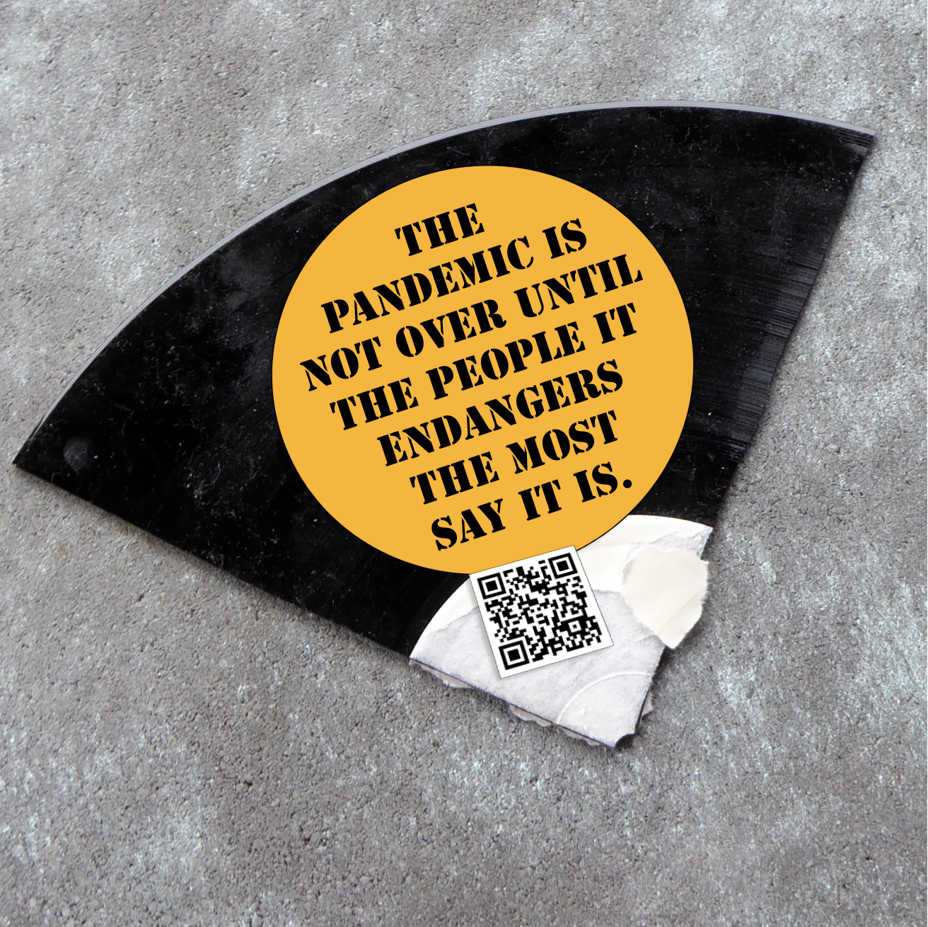 A shard of a record with a sticker on it that reads "The pandemic is not over until the people it endangers the most say it is. Next to it there's a QR-code that leads to our zine: An Open Letter to our Comrades